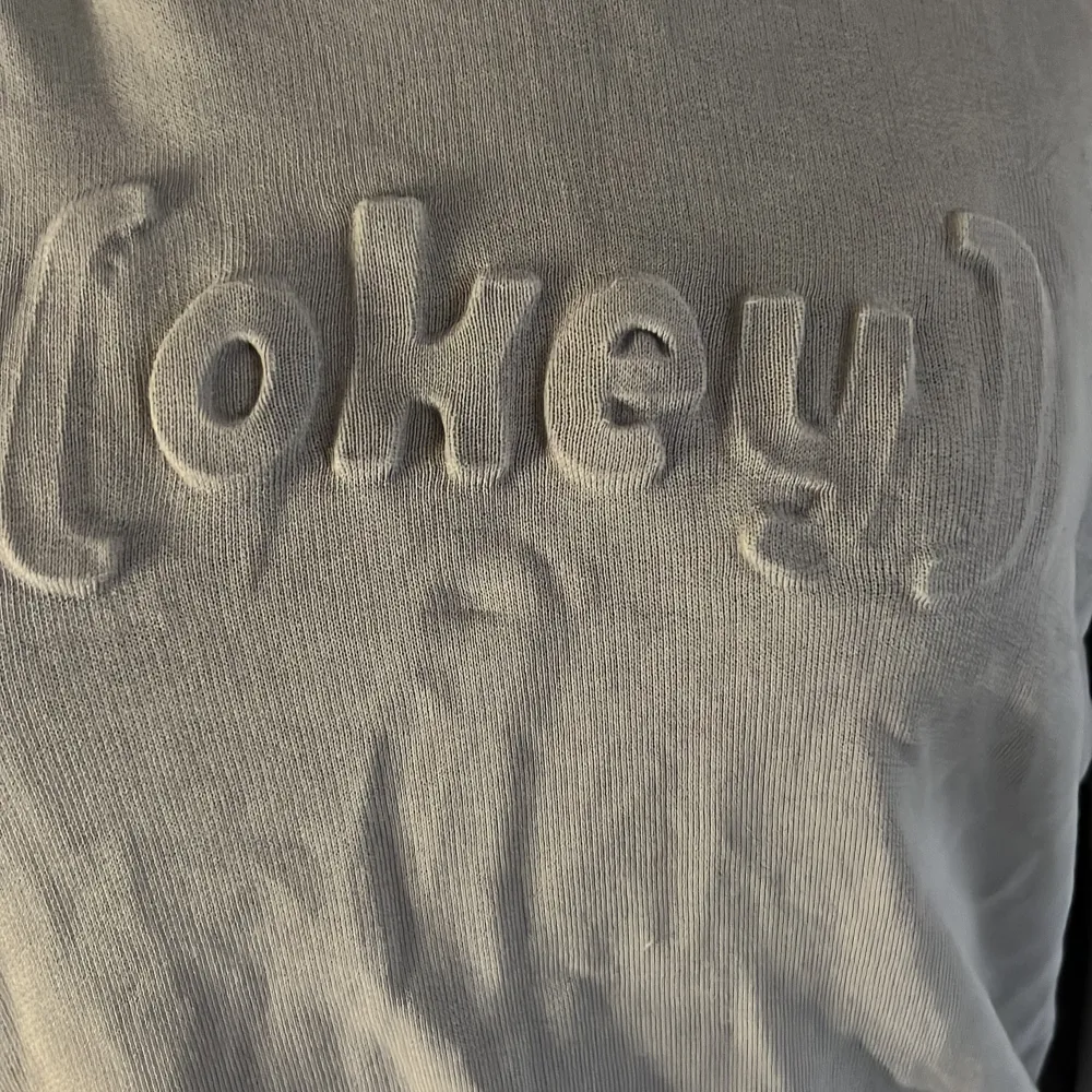 En beige hoodie från Lindex med texten 'okey' i relief på framsidan. Hoodien har långa ärmar och en ribbstickad nederkant samt muddar vid ärmslut.. Tröjor & Koftor.