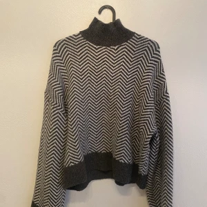Stickad tröja - En grå och vit färgad stickad tröja. Andvänd 1 gång. Hög krage med lite ”oversized” stil. 
