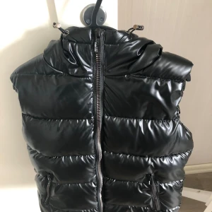 Vinterfodrad väst - Oanvänd väst i svart och glansigt tyg, säljes pga felköp. Ny skick. Juniorstorlek L, motsvarar ca 164