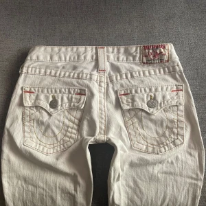 True religion jeans - Tryck gärna på ”köp”!💗 Snygga lågmidjade vita True religion jeans med gula/orange stygn! Dom är bootcut/flare och i storlek 27. Midjemått ca 37 Innerbenslängd ca 74. Har en grå fläck på vänstra lår, se bild 5! Annars toppskick!💕 jag är 165