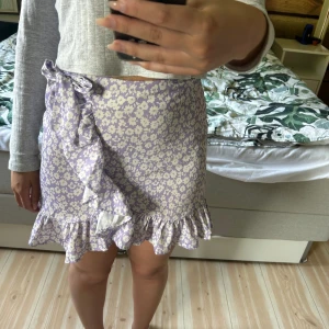 Kjol - Söt kjol med blommor på, knytbar rosett på sidan, storlek S. Dragkedja i bak, litet knäppe som ska underlätta att dra upp dragkedjan som är sönder (se bild 3) men som inte påverkar kvaliteten på något sätt.  Pris 35 kr + frakt 