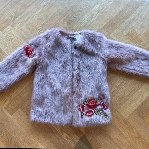Creamie Jacka - Faux Fur - Rosa - 140 - 10 år  Vacker Creamie enfärgad rosa fusk päls jacka med ros brodyrer på ena ärmen och framsidan. Creamie jackan har långa ärmar och ingen krage.  Den kan öppnas framtill med tryckknappar. Insidan har en ficka. Nästan som ny- använd fåtal gånger