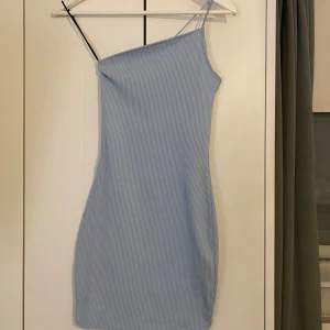 Asymmetrisk Klänning - (OBS! Ljuset lurar.Den är mer baby-ljusblå i verkligheten!) Säljer en oanvänd, ljusblå klänning. Den är perfekt till sommaren till finare tillfällen eller bara som en vardagsklänning. 