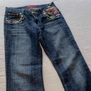 Vintage lågmidjade bootcut jeans - Jättesnygga lågmidjade jeans med blomdetaljer på Säljer dem pga att dem inte kommer till användning! 