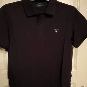 Piké-tröja Gant - Svart piké-tröja från Gant med ett märke på vänster bröst samt två knappar upptill. Fint skick.