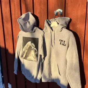 En grå hoodie i unisex modell, med ett tryck på ryggen. Helt nya och oanvända. (Den kommer inte med TT trycket på framsidan) Går att få ett inbroderat citat på armen utan extra kostnader.