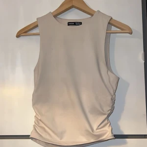 Rynkad Topp - Beige tanktopp som är rynkad på sidorna. Har aldrig använt toppen så den är så gott som ny👍🏼