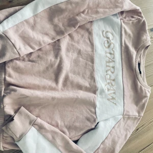 Collegetröja  - Måttligt använd collegetröja. Rosa/vit. Hel och ren. Inga fläckar. Oklart märke.  Passar tjej 11-13 år ca. 