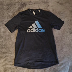 Adidas t-shirt - Mörkblå Adidas t-shirt, perfekt till gymmet eller annan fysisk aktivitet. Stort blå vity tryck på framsidan och litet vitt på nacken. Storlek medium. Material: 65% polyester och 35% bomull. Skriv vid minsta fundering eller fråga 🤝