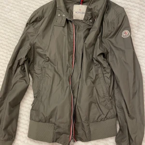 Moncler jacka - Bra skick men 2 små hål på ena axeln. Äkta moncler med märket på vänster arm. Har inte kvitto tyvärr. Färgen är lite grå/grön.