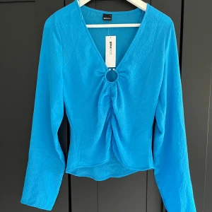 Blå blus - Blå blus som aldrig är använd, har prislapp kvar.  Lite genomskinlig. Metallring i fram.  Nypris 359 kr