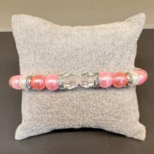 Handgjort pärlarmband med rosa, vita och genomskinliga pärlor, med blingiga mellanplattor och silvrigt spänne. Justerbar passform mellan 17-21 cm.