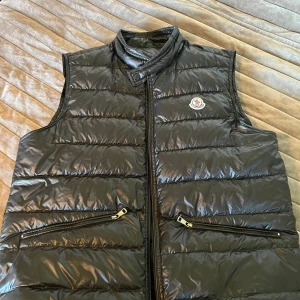 Moncler Gui Down Väst -  Lättviktsdunväst i superfint skick! Tycker inte den är stor i storleken. Sonen som har XL har haft den.  Jag som har stl M kan ha den utan att den ser ”stor” ut.  