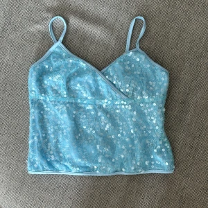 Ljusblå paljettprydd linne topp - En ljusblå linne topp med smala axelband och paljettprydd yta. Toppen har en omlott-design framtill och är tillverkad i ett glittrande material💕