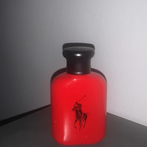 Röd parfymflaska från Ralph Lauren - Säljer en snygg röd parfymflaska från Ralph Lauren. Flaskan har en stilren design med en svart kork och en svart logotyp av en häst och ryttare på framsidan. Perfekt för dig som vill ha en elegant och maskulin doft. Köp direkt eller ge prisförslag 💛