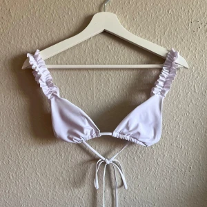 Vit bikiniöverdel med volangdetaljer - Säljer en superfin vit bikiniöverdel med volangdetaljer på axelbanden. Den har en enkel och stilren design med knytning i ryggen. Perfekt för sommarens alla stranddagar! 💖