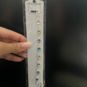 Färgglatt armband från Fashion Jewelry - Säljer ett superfint armband från Fashion Jewelry. Det har en rad med färgglada stenar i olika former och färger som blå, grön och rosa. Perfekt för att liva upp vilken outfit som helst! 💎✨