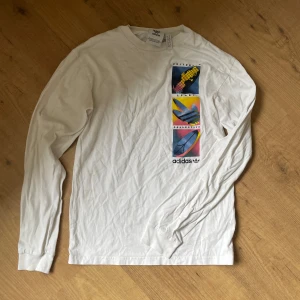 Vit långärmad tröja från Adidas - Säljer en vit långärmad tröja från Adidas. Tröjan har ett coolt tryck. storlek xs