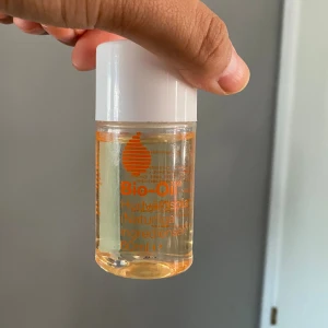 Bio-Oil Hudvårdsolja - Säljer en flaska Bio-Oil Hudvårdsolja på 60 ml. Denna olja är känd för sina återfuktande och vårdande egenskaper, perfekt för att förbättra utseendet på ärr, bristningar och ojämn hudton. Flaskan är genomskinlig med en vit kork och orange text.