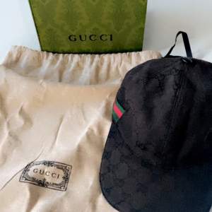 Säljer en snygg svart keps från Gucci. Kepsen har en diskret mönsterdesign och en grön och röd rand på sidan. Perfekt för att ge din outfit en lyxig touch. Kommer med originalförpackning och dustbag.