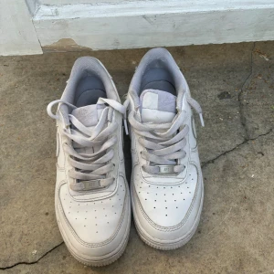 Vita Nike Air Force sneakers - Säljer ett par vita Nike Air Force One sneakers i storlek 38,5 Skorna är i välanvänt skick men fortfarande bekväma och snygga. Perfekta för vardagsbruk eller träning. De har klassisk snörning och är tillverkade i syntetmaterial.