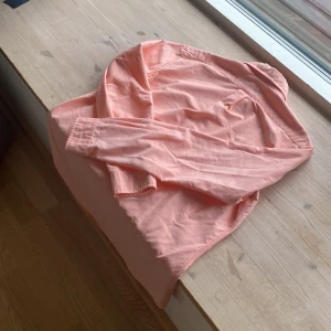 Rosa skjorta från Ralph Lauren - Säljer en snygg rosa skjorta från Ralph Lauren i storlek M. Skjortan är långärmad och har knappar hela vägen ner. Den är gjord av bomull och har en broderad logga på bröstet. Perfekt för både vardag och fest!