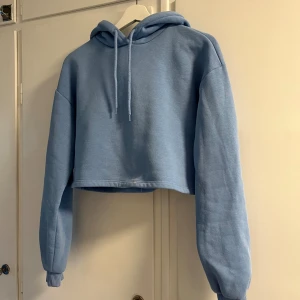 Ljusblå croppad hoodie - Säljer en superfin ljusblå croppad hoodie. Den är perfekt för en chill dag eller när du vill vara bekväm men ändå snygg. Den är i bra skick men har några små blekningsfläckar här och var som knappt syns.💙