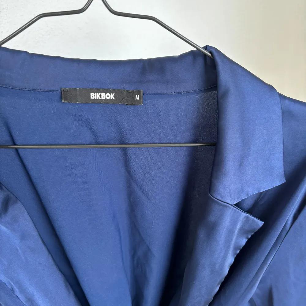 Märkblå silkes-liknande topp med skärp i M. Skulle säga att den passar S-M i storlek.  En av ”bälthållarna” har åkt av, men det gör inte så mycket då det finns en kvar som håller upp skärpet.. Blusar.