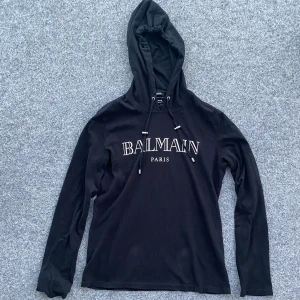 BALMAIN LOGO HOODED T-SHIRT - Äkta Balmain Paris hooded t shirt som har egenskaper av både en t-shirt och en hoodie. Asfet och i 10/10 condition. Använd bara ett fåtal gånger. Köpt på luisaviaroma hemsida. Storlek: M. Hör av er vid eventuella frågor!!