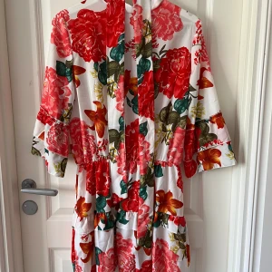 Blommig klänning med tillhörand bälte i midjan - Använd fåtal gånger, ser oanvänd ut. Tillhörande bälte i midjan, som hänger på galgen. Vet ej märke då den är köpt utomlands. Stlk 38 kanske en 40