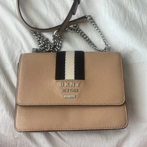 DKNY väska - DKNY Väska köpt från Åhléns för ca 3000kr. Använd och kedjan har tappat färgen lite som ni kan se på bilden därav säljs den billigt