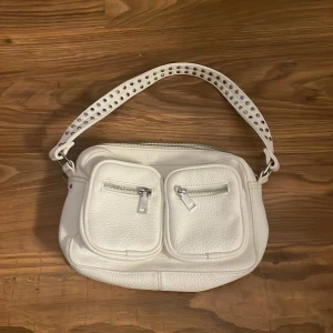 Noella väska - Säljer denna helt oanvända normal väskan då den aldrig kommit till användning. Saknar ett långt band bara, annars toppen skick. Denna noella väska är vitt i läder tyg ungefär och är noellas medel storlek. Väskan rymmer väldigt mycket. 