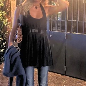 Halterneck topp - Svart halterneck topp med knyte i nacken, dragkedja på sidan och en ”rosett” framti, som ny