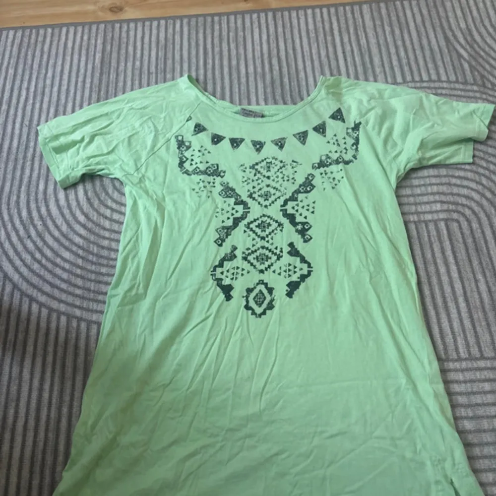 En grön t-shirt från Cellbes med ett dekorativt mönster i mörkare grönt på framsidan. T-shirten har korta ärmar och en rund halsringning.. T-paidat.