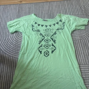 Grön t-shirt från Cellbes - En grön t-shirt från Cellbes med ett dekorativt mönster i mörkare grönt på framsidan. T-shirten har korta ärmar och en rund halsringning.