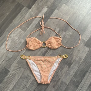 Bikini från Victoria’s secret  - En jättefin bikini överdel och underdel från Victoria’s secret i färgen rosa och brons med guld kedjor på underdelen och en guld ring på mitten av överdelen.(Storlek S) Har använt den endast en gång! Den är perfekt för sommaren när man ska bada osv.💗