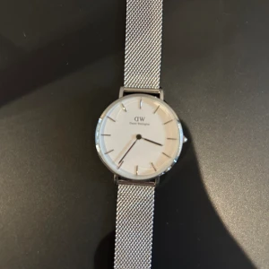 Daniel Wellington klocka  - En silvrig Daniel Wellington klocka i mycket fint skick. Klockans längd ska gå att reglera. Klockan fungerar och klockans ask medföljs vid köp. Nypris 1699kr