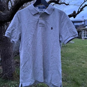 Ralph Lauren Piké - Grå - Säljer min helt nya Ralph lauren pike. Lapparna kvar på den. Säljer då den är för liten för mig. Storlek M. Perfekt till sommaren. QR kod i nacken som scannar. Kan skicka fler bilder eller svara på frågor i DM! 🔥🙌