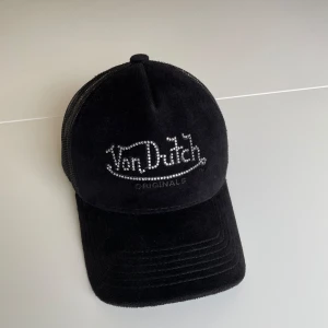 Svart keps från Von Dutch - Säljer en svart keps från Von Dutch i nyskick, dekorerad med Von Dutch-logotypen i glittriga stenar. 