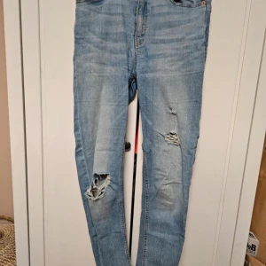 Blå jeansbyxor från 157 - Ett par blå jeansbyxor från märket Lager 157 i storlek S. Byxorna har en skinny passform och är dekorerade med slitningar på framsidan. De har en hög midja och är tillverkade i ett stretchigt material för extra komfort.