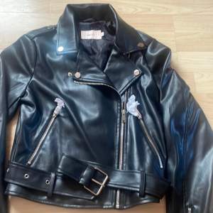 Grymt Snygg svart Biker Jacket med bälte i midjan från Nelly. Jackan har dragkedjor framtill och på fickorna. Den har även en dragkedja på varje ärm.  Jackan är oanvänd . Nypris 679kr