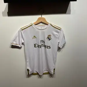 Säljer en replika av Hazard Real Madrid tröja från säsongen 2019/20. Storlek: S. Tröjan har använts men är i mycket gott skick. Den vita designen med gulddetaljer speglar klubbens elegans och Hazard's nummer 7 pryder ryggen. Perfekt för samlare eller