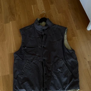 Väst ut och in - Denna väst är två västar i en då den går att vända ut och in. Ena sidan soldatgrön och andra sandbeige. En väst med swag. Storlek M Känns lite skate. Har några små röda fläckar på två ställen, annars bra skick.