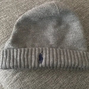 Grå polo mössa -  polo mössa är en snygg och sportig accessoar som kan ge en touch av elegans till din outfit. Den är vanligtvis tillverkad av kvalitetsmaterial och har ofta en diskret logotyp eller emblem på framsidan. En polo mössa kan vara ett bra val för en mer