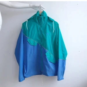 Asics vindjacka - Retro vindjacka/windbreaker från Asics med silvriga sömmar, fyra fickor och avtagbar luva. 