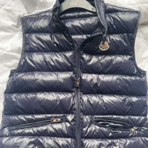 Moncler Gui Väst - Västen är i bra skick som ny och den passar inte mig för att jag är smal så om du är smal jag rekomenderar att inte köpa den. Passar bättre om man är lite bred. Den passar om man är 157-165 något sånt👍