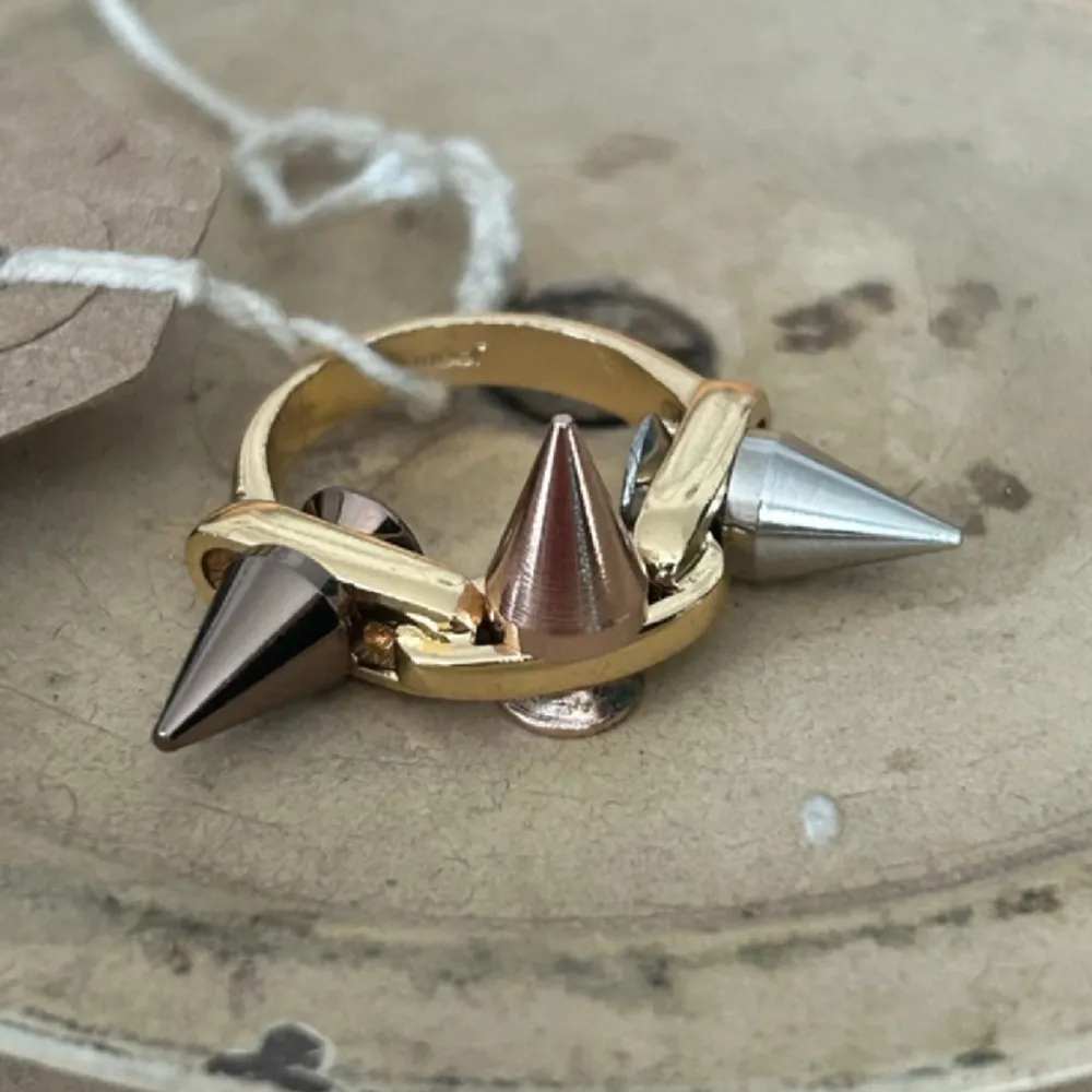 Unik guldfärgad ring från joomi lim med nitar i färgerna silver, brons och rosé. Skulle säga att den passar på långfingret eller tummen. Det är rostfritt stål.. Accessoarer.