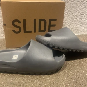 Yeezy Slides - Grå - Gråa yeezy slides med förpackning som ingår  Fint skick och använda. Men inga defekter eller skador på skorna.