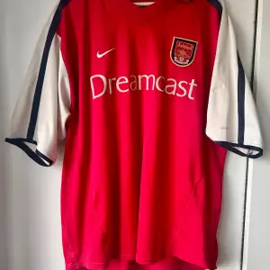 En äkta Arsenal tröja från 00/01. 9/10 skick. Ända defekten är det som lossnat vid M:et (se bild) men det är inget som märks vid användning. Storlek XL. Kan vara svårt att sen produktkoden men den är : F0ORE