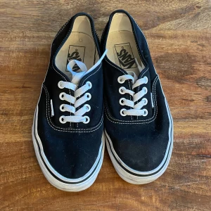 Svarta Vans sneakers - Ett par svarta Vans sneakers med vita snören och vit sula. Skorna har en klassisk design med låg profil och är i bra skick.